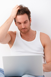 Athletic young man using laptop, browsing internet.